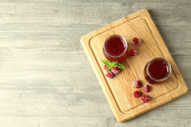 Glass jars of raspberry jam with ingredients on wooden board