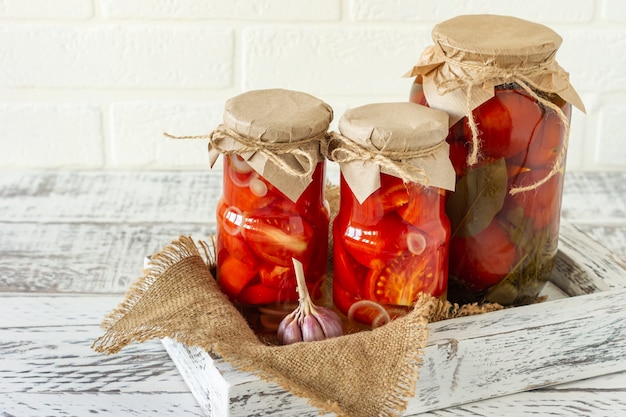 Glass jars with canned tomatoes with garlic and pepper. Fermented food on a white wooden background.