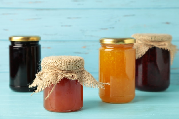 Glass jars with different kinds of jam on blue background. Top view