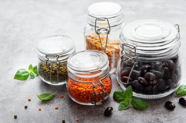 Glass jars with different types of legumes on a gray concrete surface