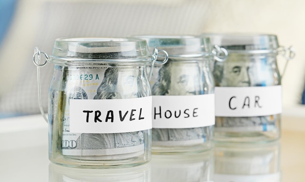 Glass jars with dollar banknotes for car house and travel on a table