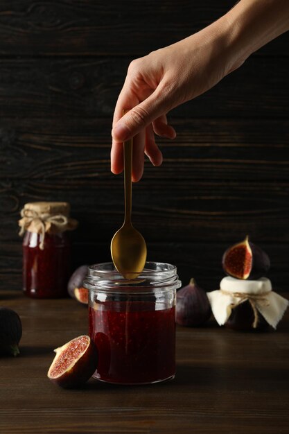 Vasi di vetro con marmellata di fichi interi e tagliati a fette mano femminile con cucchiaio su sfondo di legno