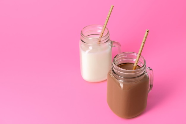 Glass jars with flavoured milkshakes against pink background