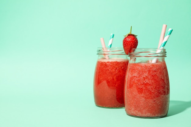 Glass jars with strawberry cocktail on mint background