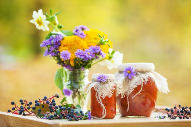 Glass jars with tasty apricot jam and bouquet of autumn flowers on a table. Autumn time