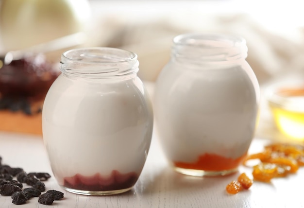 Glass jars with tasty yogurt and jam on white wooden background