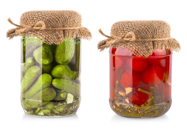 The glass jars with tomatoes and cucumbers with burlap lid on a white background