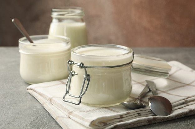 Glass jars of yogurt, spoons and napkin on gray