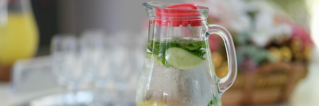 Glass jug of detox water with lemon and cucumber standing on table closeup