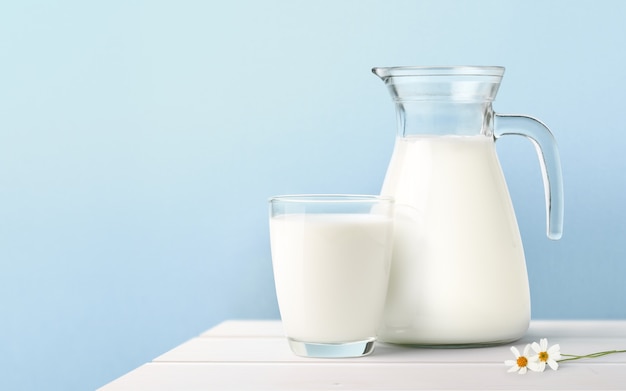 Glass and Jug of fresh milk on white wooden table.