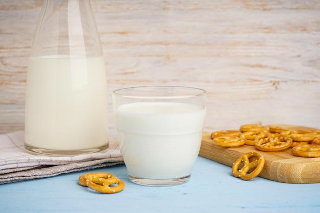 Glass and jug of fresh milk on wooden table against color background Closeup