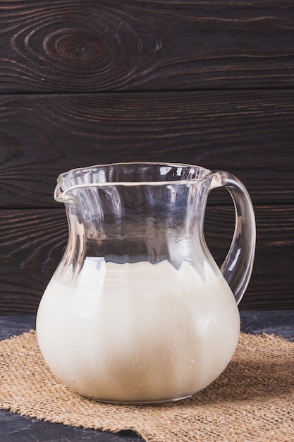 Glass jug full of fresh milk on a wooden dark wall