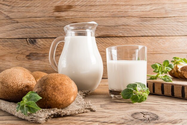 A glass jug and a glass of vegetable vegan potato milk potato tubers leaves close angle wooden brown background of boards