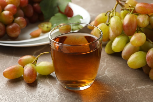 Стакан сока и тарелка с виноградом на сером