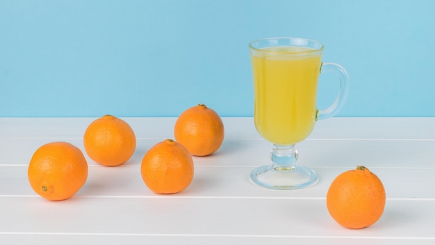 A glass of juice and tangerines scattered on a wooden table