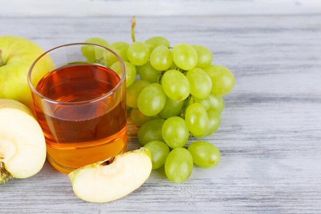 Glass of juice with fresh grape and apples on grey wooden table