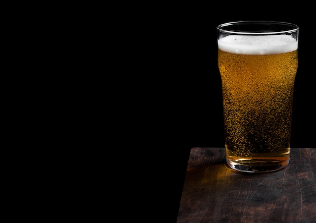 Glass of lager beer with foam and bubbles on vintage wooden board on black.