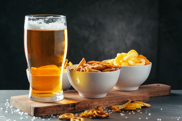 Glass of lager beer with snack bowls on dark stone 