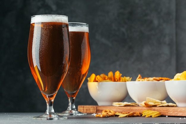 Glass of lager beer with snack bowls on dark stone 