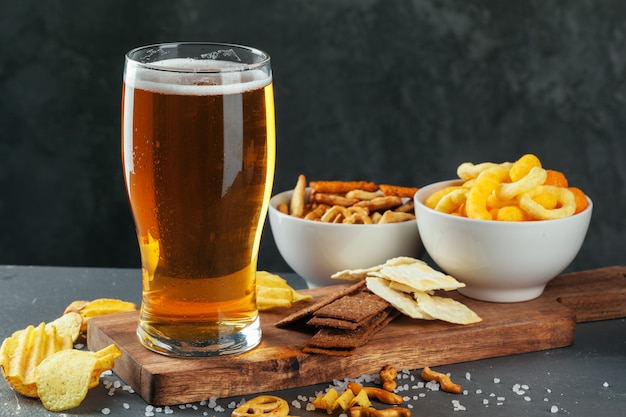 Glass of lager beer with snack bowls on dark stone 