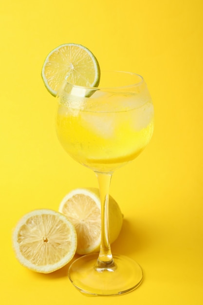 Glass of lemon cocktail and ingredients on yellow background