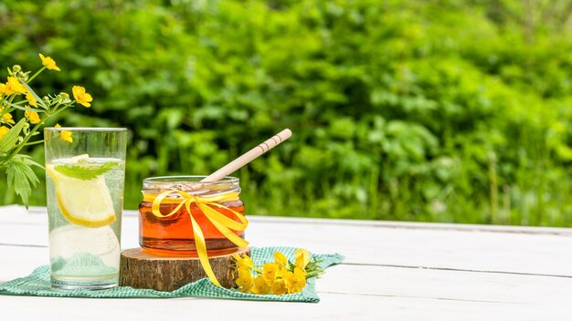 A glass of lemonade and a jar of honey in nature.