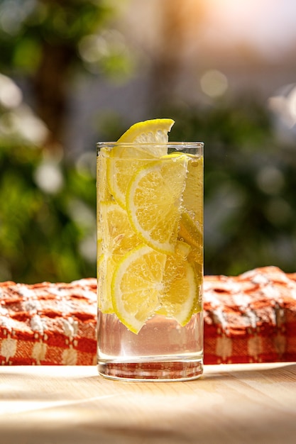 Glass of lemonade with lemon on sunny garden.