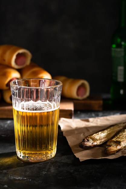 A glass of light beer and two dried fish on a black table