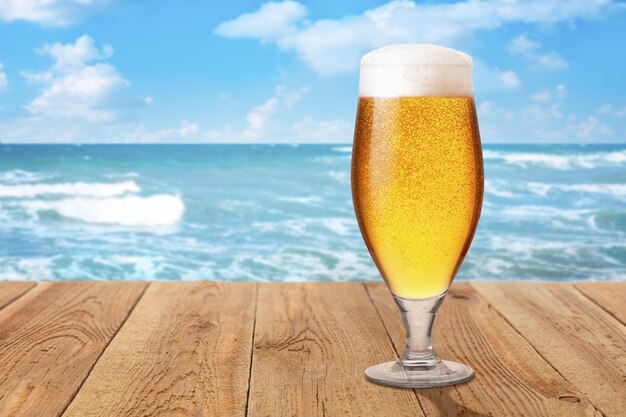 glass of light beer with foam and bubbles on wooden table against sea