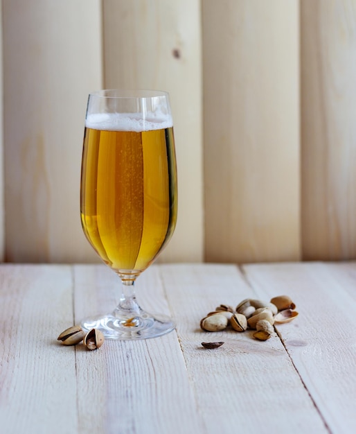 A glass of the light beer on the wooden background with pistachios