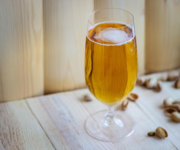 A glass of the light beer on the wooden background with pistachios