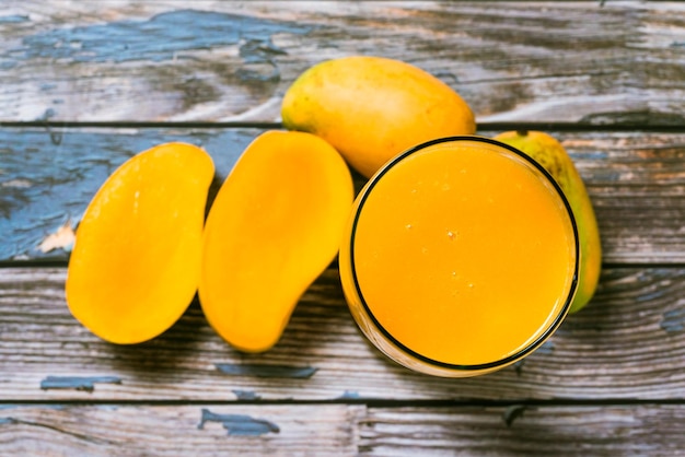 Glass of mango juice and sliced mangoes on wooden table. Colorful scene.