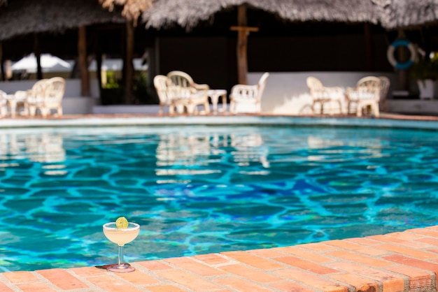 Glass of margarita cocktail with blue swimming pool background