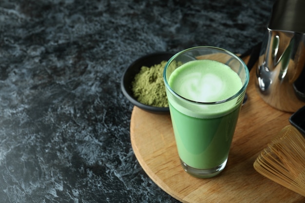 Glass of matcha latte and accessories for making on black smokey table