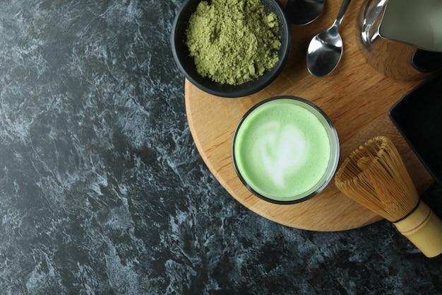 Glass of matcha latte and accessories for making on black smokey table