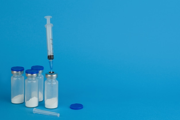 Glass medical ampoule vial for injection with syringe. Medicine dry white drug penicillin powder or antibiotic. Bottles ampule with aluminum cap on backgrounds blue. Virus salvation. Copy space.