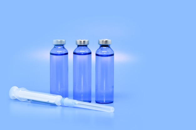 Glass medical ampoules and syringe, light blue background. Concept: medicine, injections, vaccine