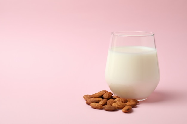 Glass of milk and almonds on pink background