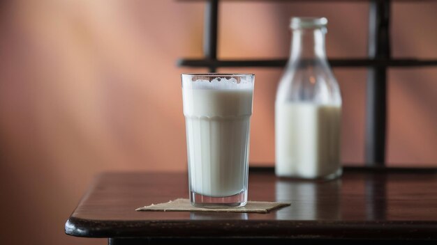 Foto un bicchiere di latte e una bottiglia sullo sfondo