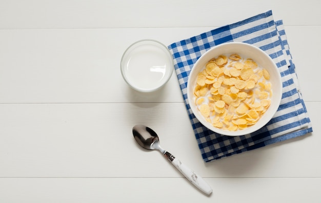 Glass of milk next to bowl of cereals on cloth