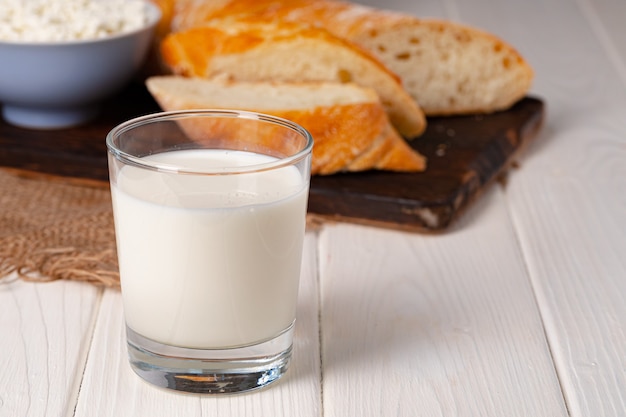 Glass of milk, bowl of cottage cheese and bread on table