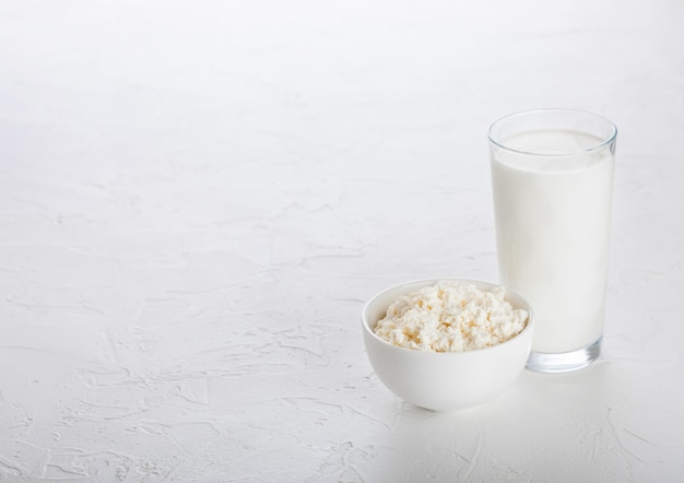 Glass of milk and bowl of cottage cheese on white stone kitchen table.