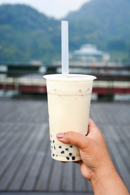 Glass of milk bubble tea with tapioca pearls in tourist hand with sun moon lake background