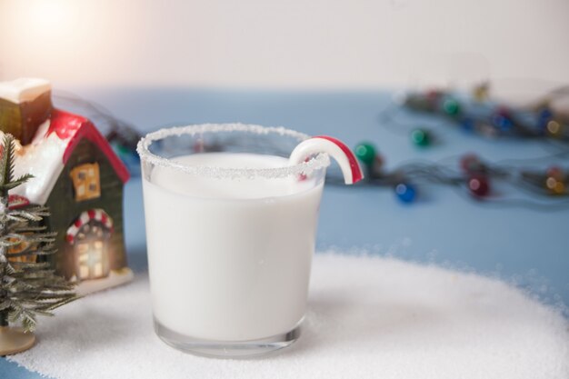 Glass of milk, candy cane, house and christmas tree miniatures on blue