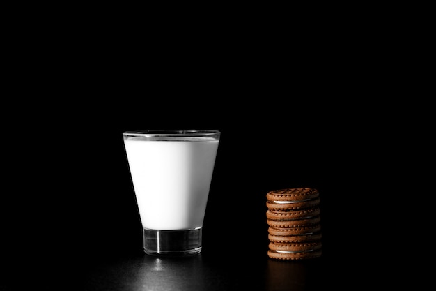 Glass of milk and chocolate cookies on black