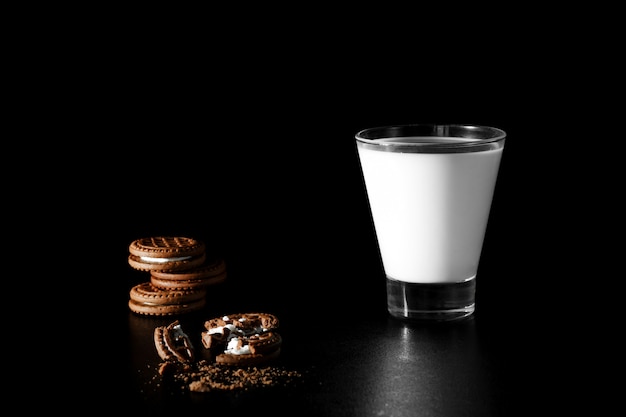 Glass of milk and chocolate cookies on black 