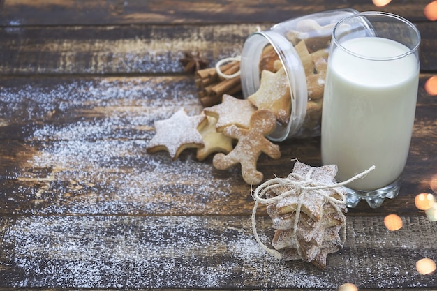 Photo glass of milk and christmas cookies on brown wooden table with christmas lights