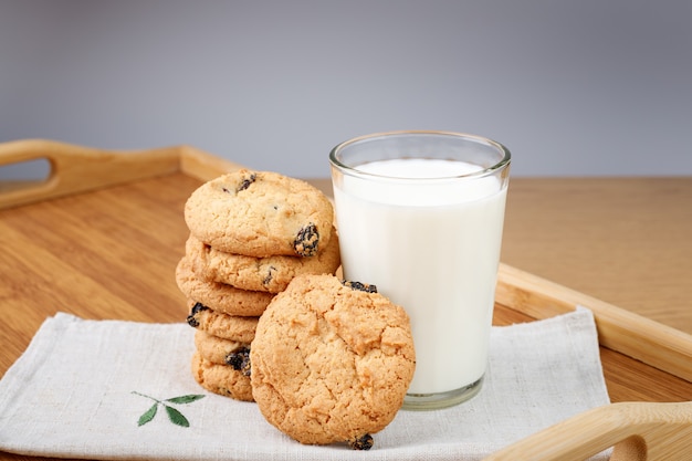 Photo a glass of milk and cookies with raisins on a wooden tray