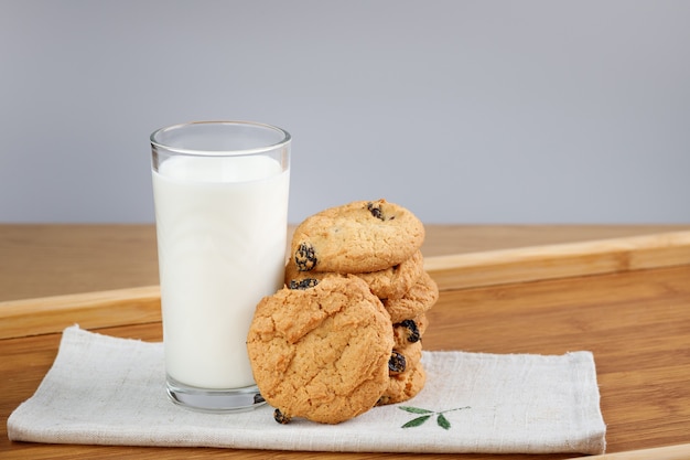 Photo a glass of milk and cookies with raisins on a wooden tray