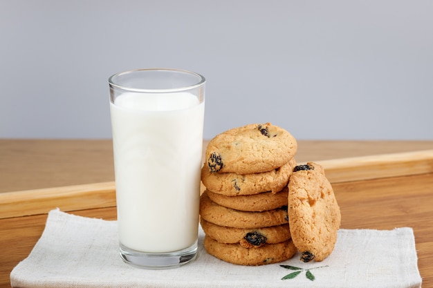 A glass of milk and cookies with raisins on a wooden tray